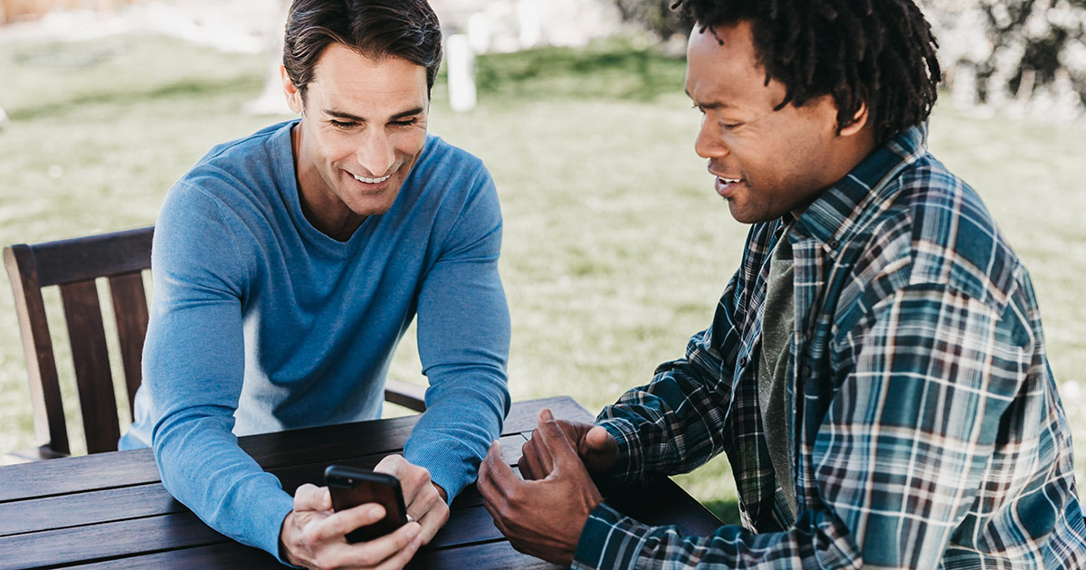 two friends talking outside at picnic table with phone