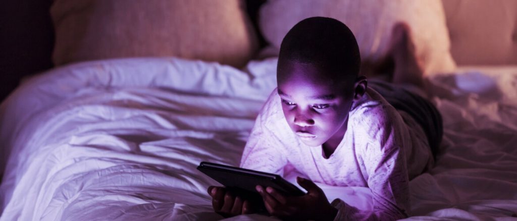 boy lying in bed looking at a tablet