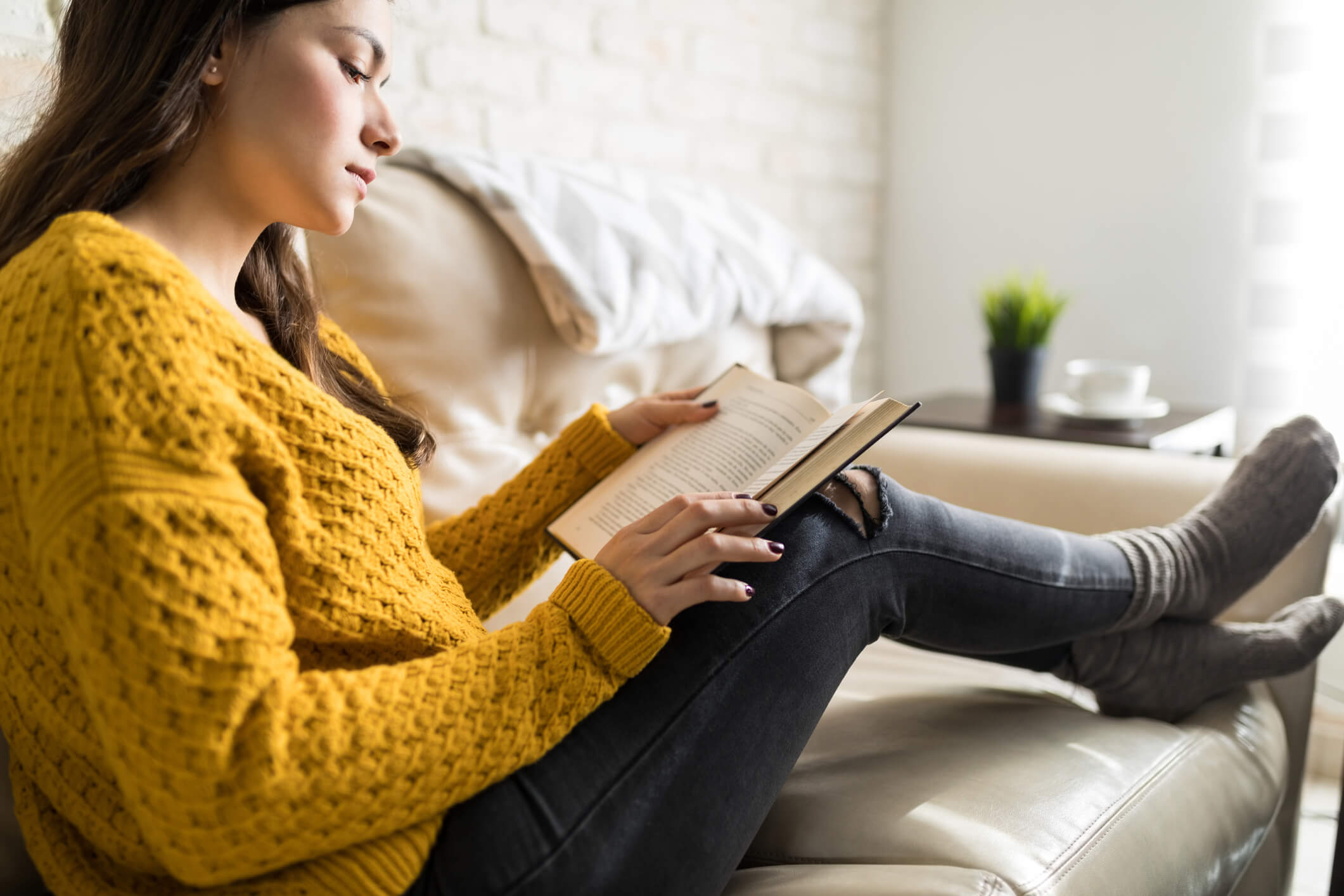 A young woman sitting on a couch and reading a book.