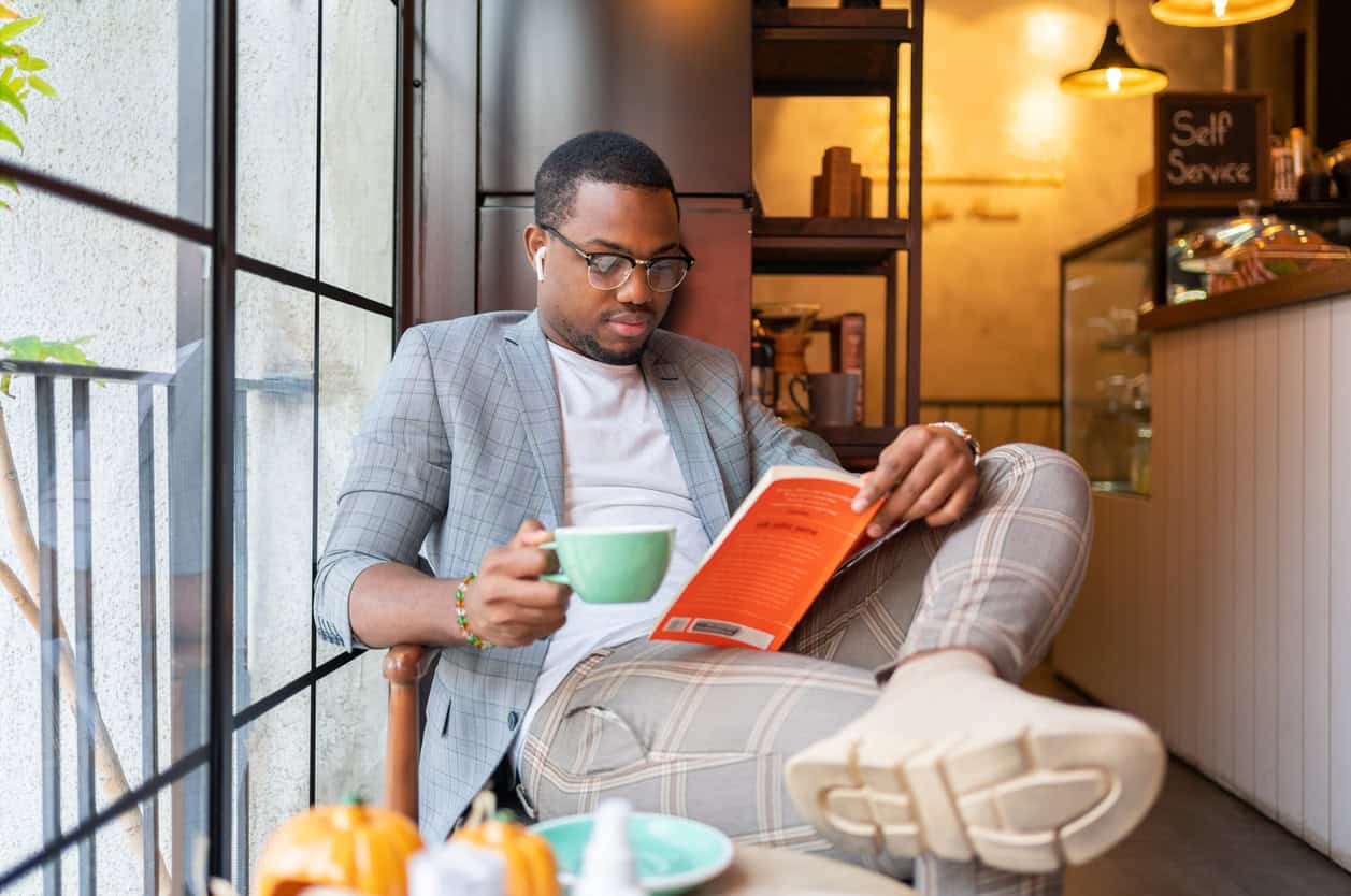 A young man reading a book at a coffee shop.