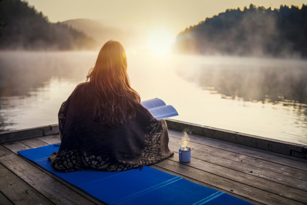 A woman sitting on a dock at sunrise and reading about sexual sanity.