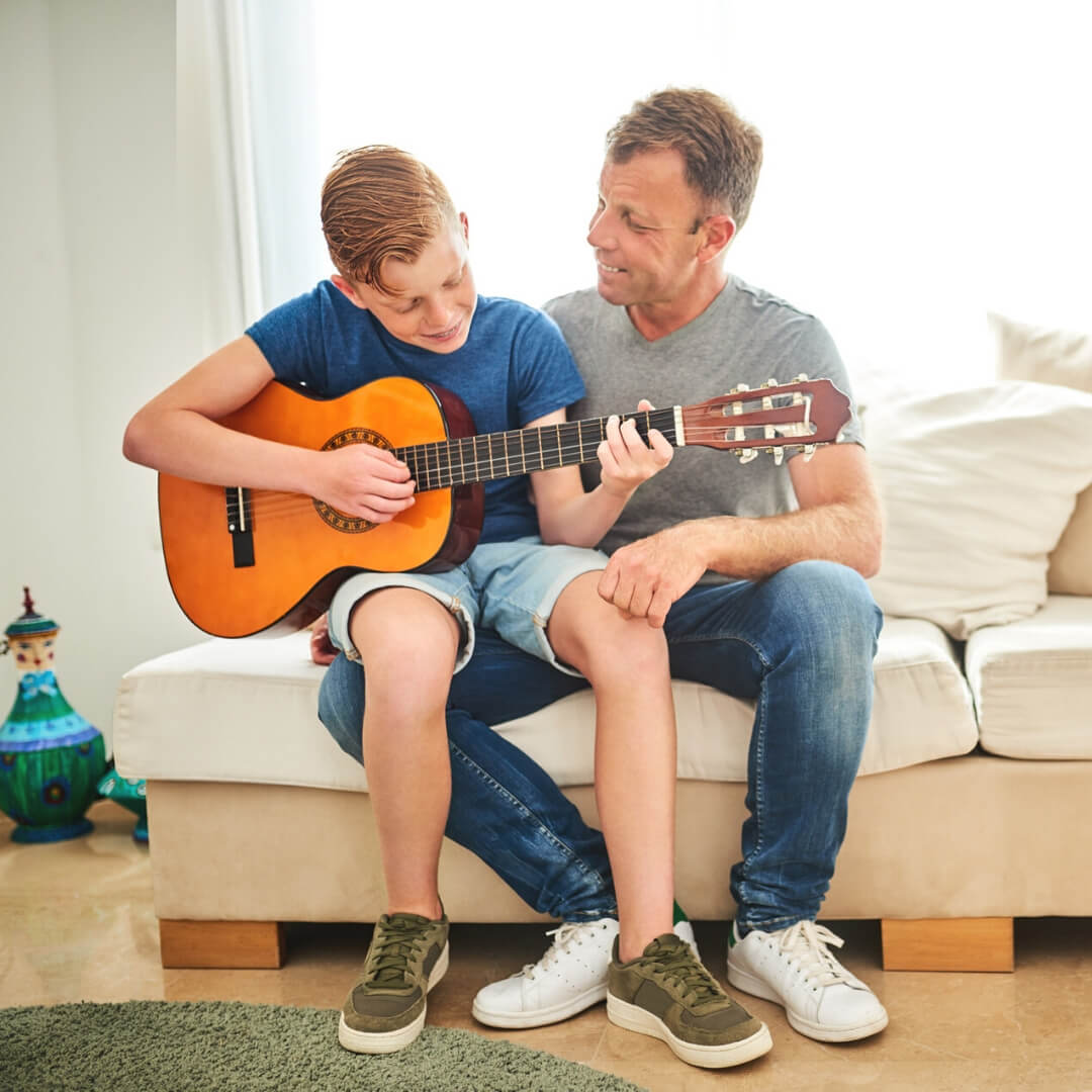 dad teaching son guitar on the couch