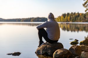 Man sitting by the shore looking at a peaceful lake.