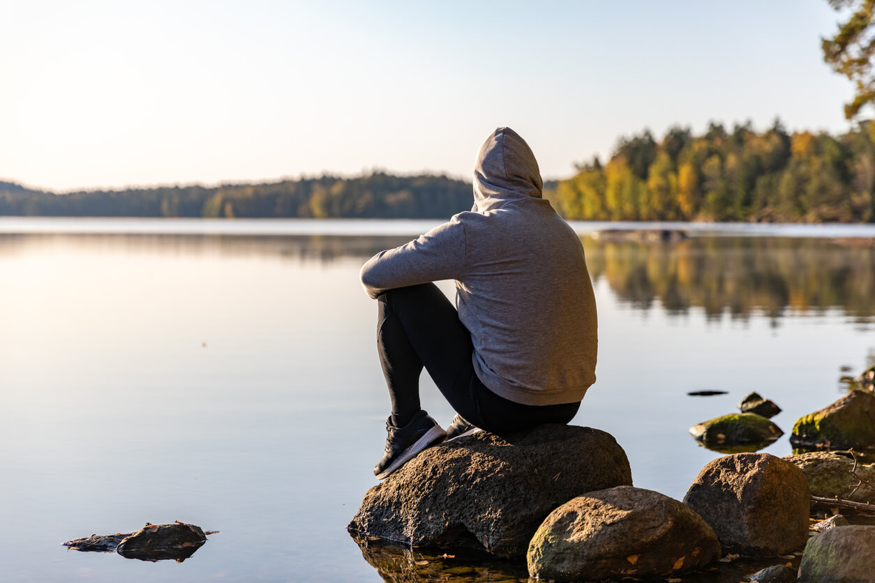 Man sitting by the shore looking at a peaceful lake.