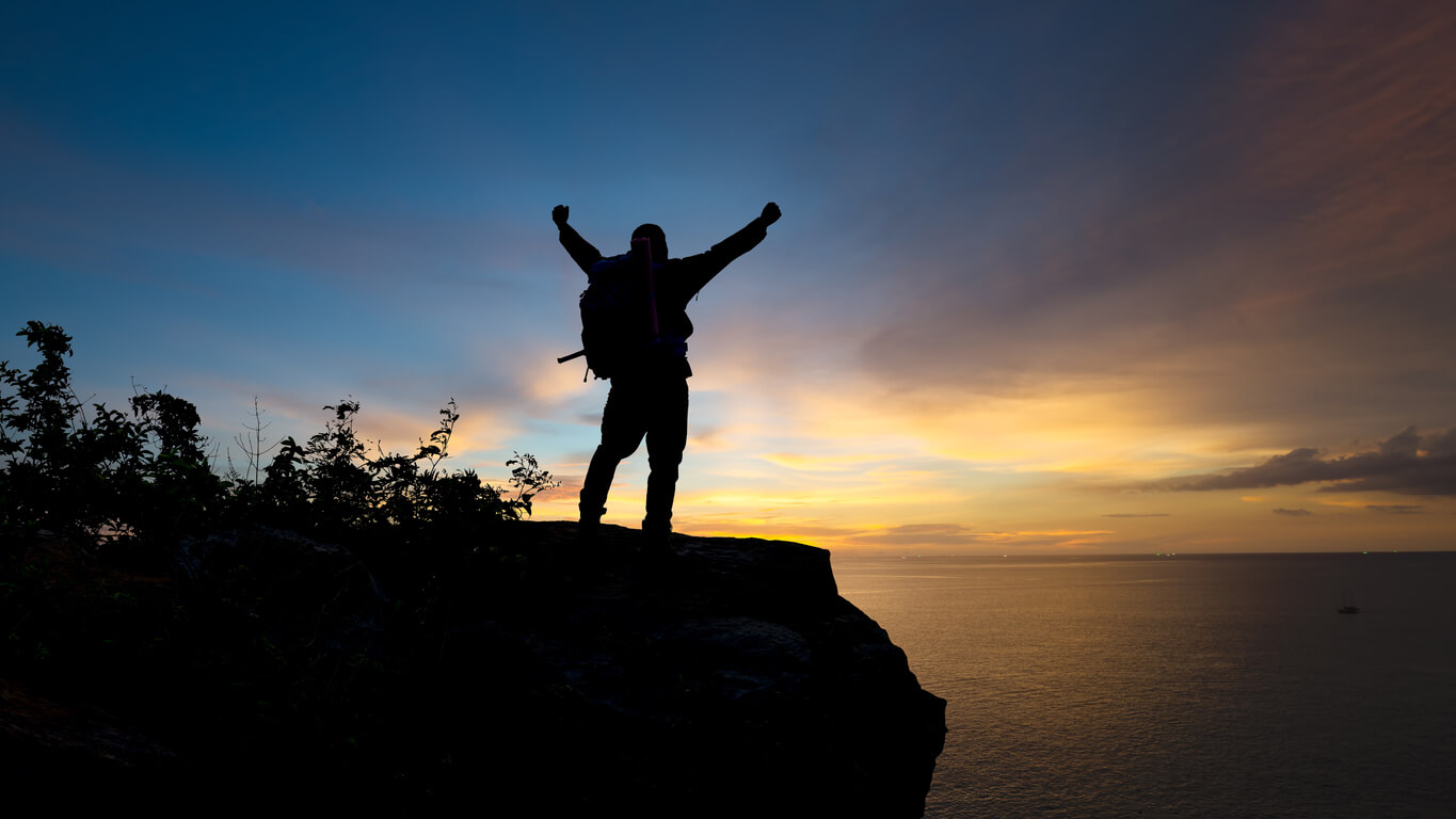 Silhouette of a hiker who has reached the summit at sunset.