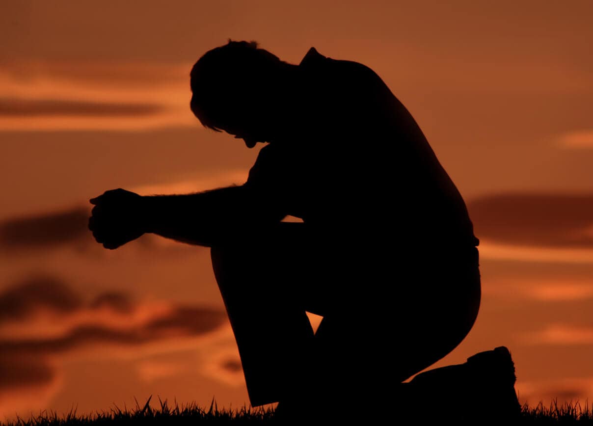 Silhouette of a man outside kneeling in repentance.