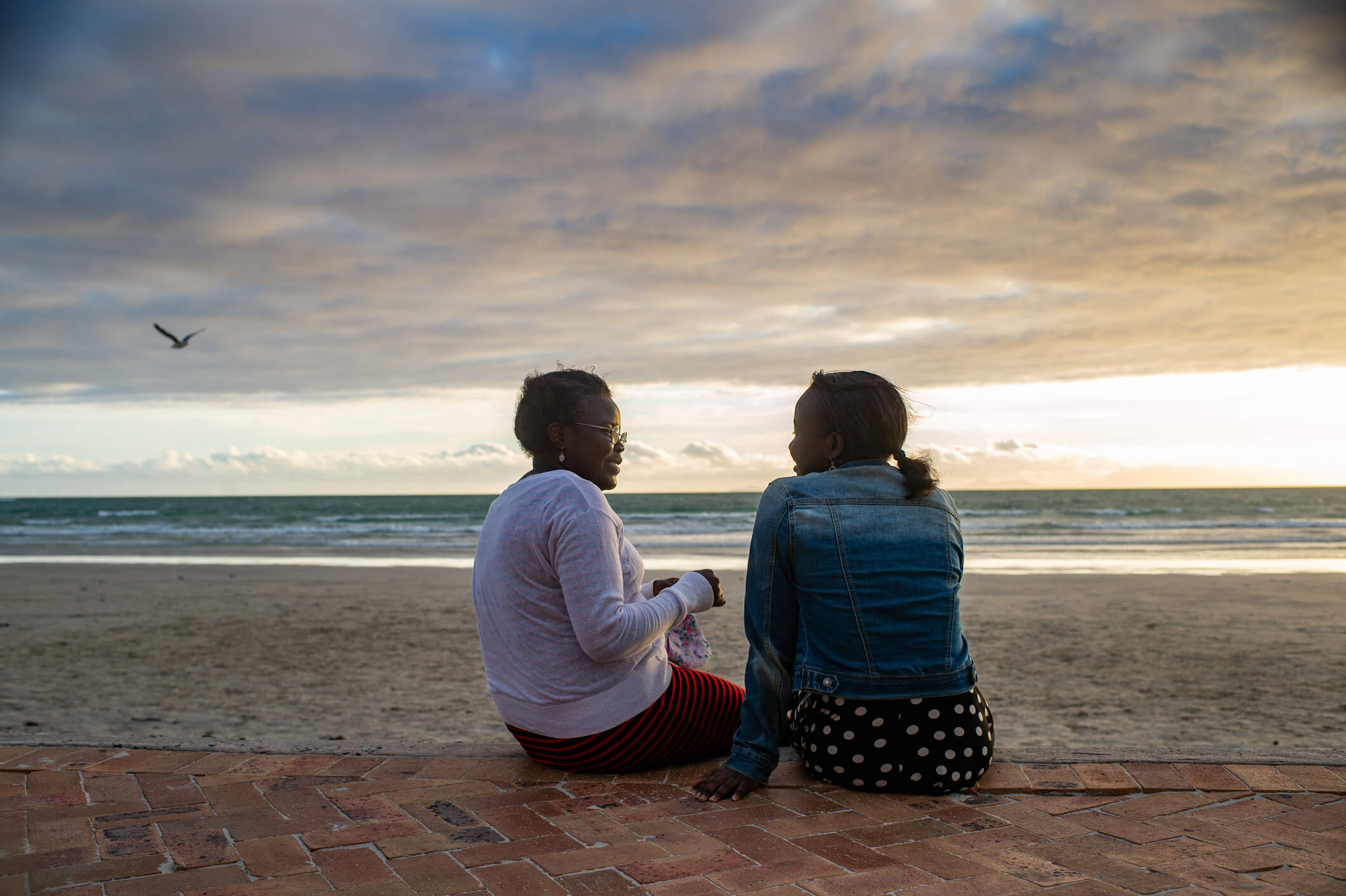 A mother and daughter sitting on the beach at sunset.