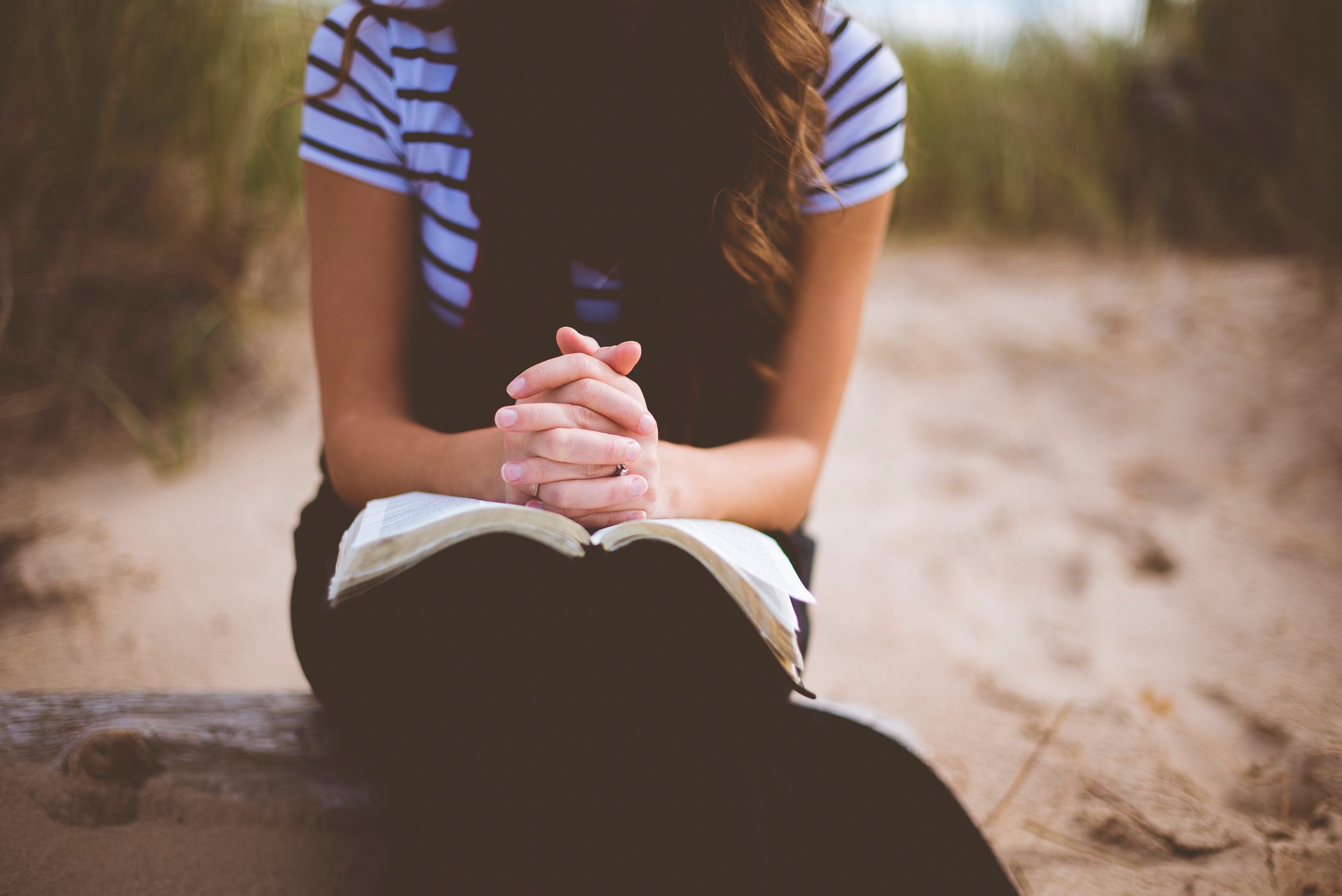 girl folding hands over bible