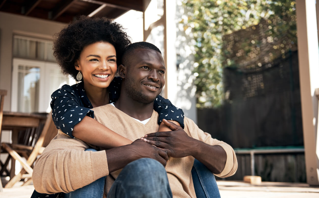 An affectionate couple sitting on a sunny front porch.