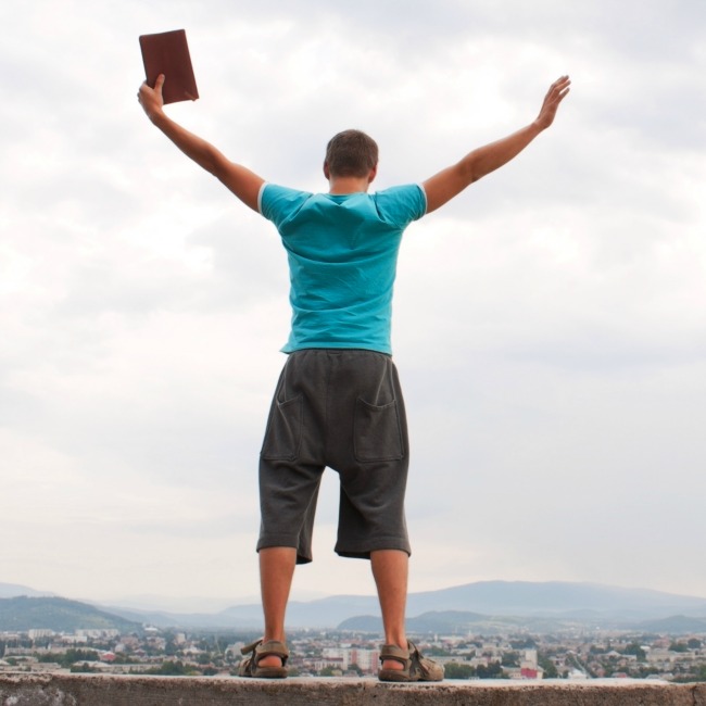 man with hands in air holding bible