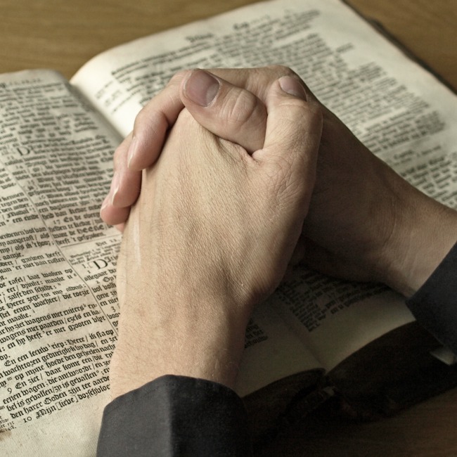 folded hands on bible