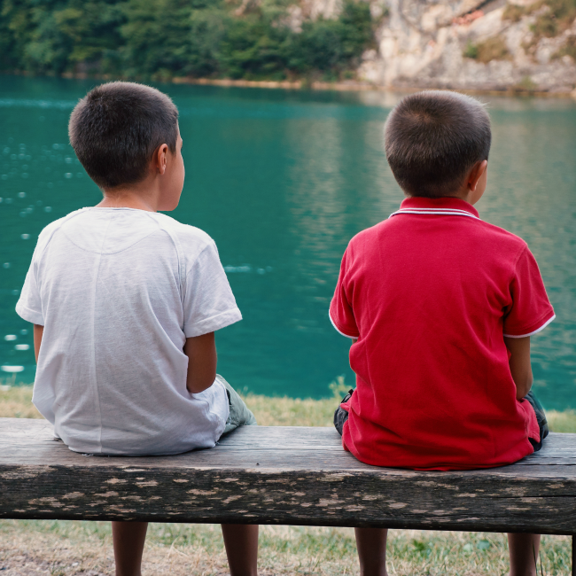 two boys sitting in front of lake