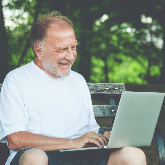 smiling man on computer on park bench