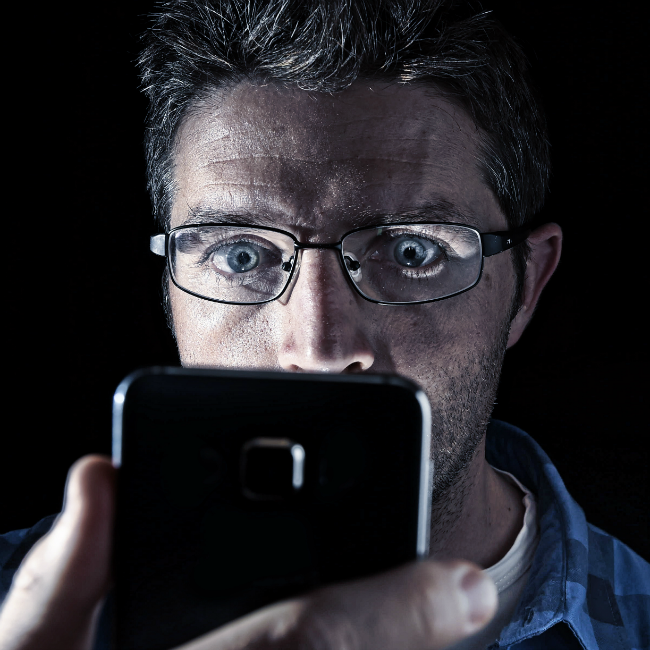 man in dark staring at phone