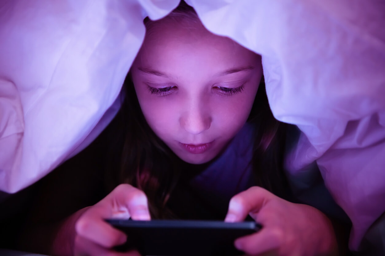 child under blankets with a phone