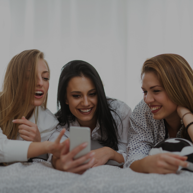 three girls laughing while looking at phone