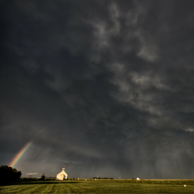 church with dark cloud and rainbow over it