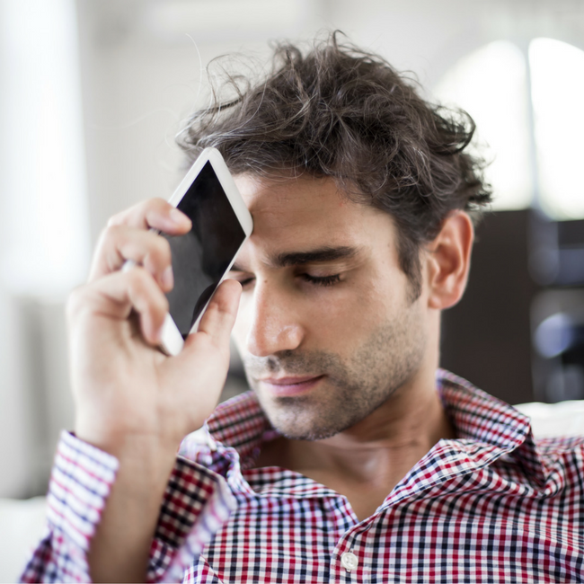 man holding phone to forehead