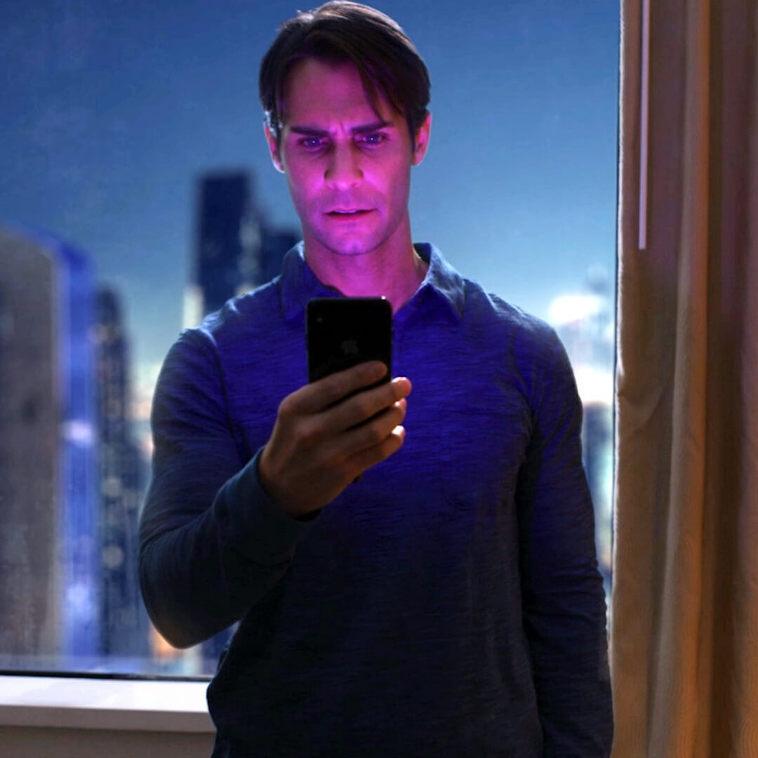 man looking at phone at night with cityscape behind him