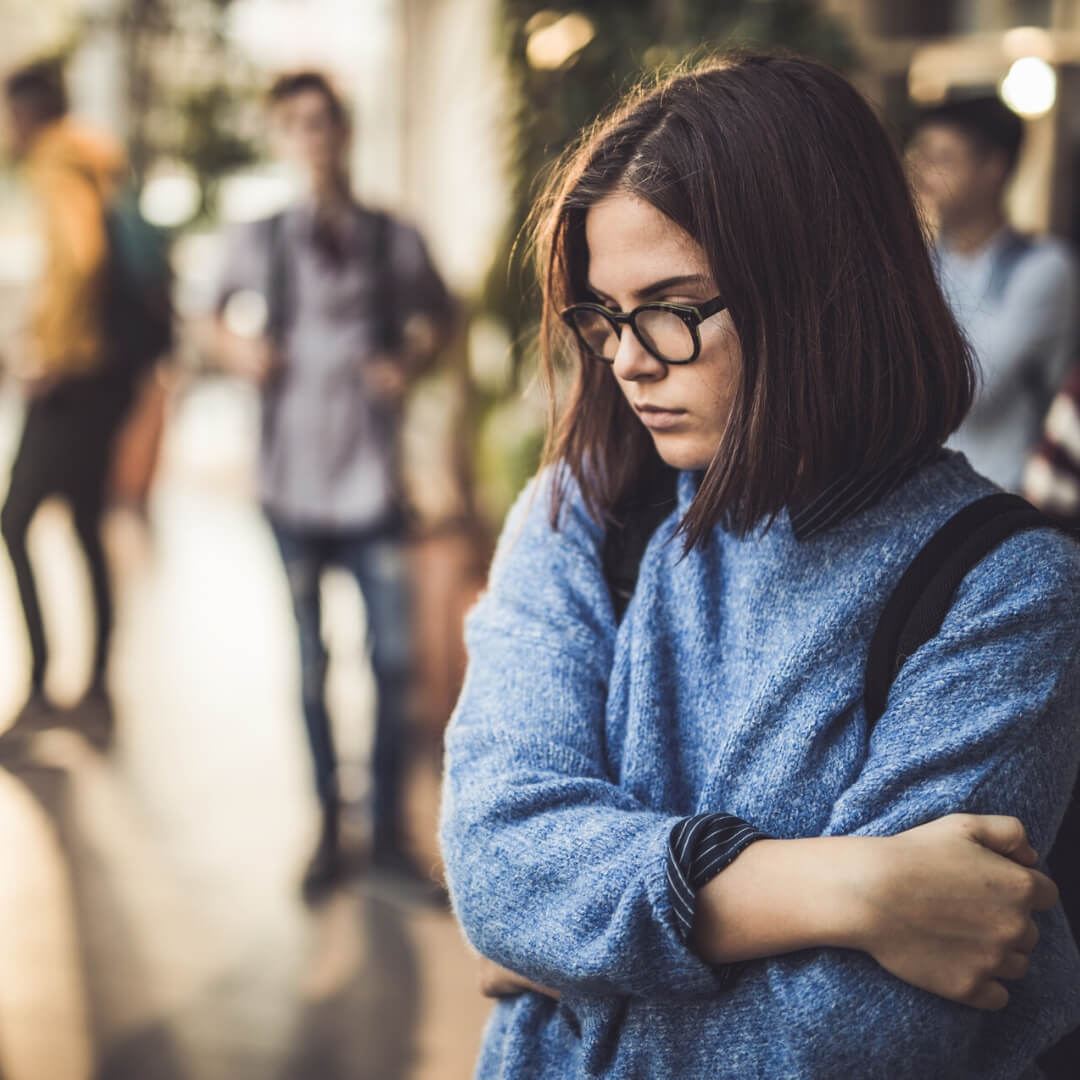 high school girl looking sad with friends in background