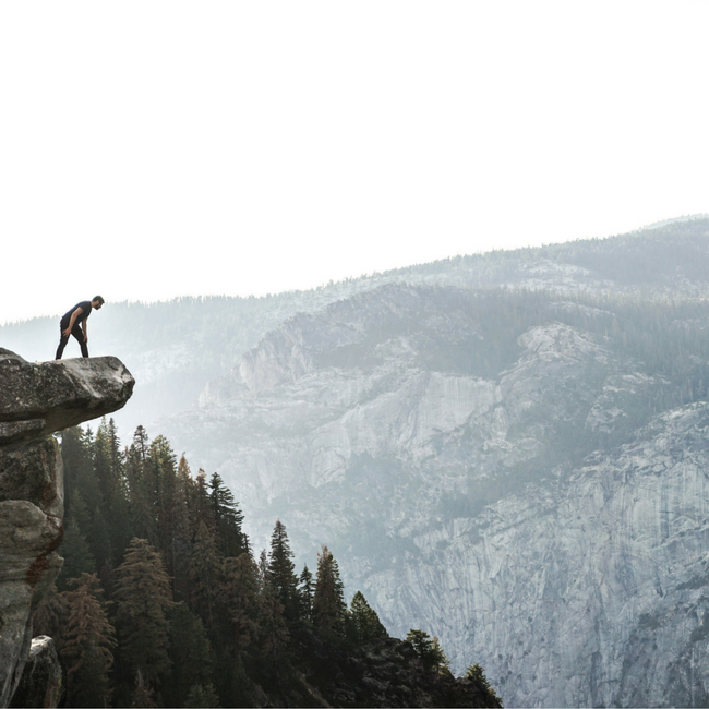 man looking off the edge of a cliff