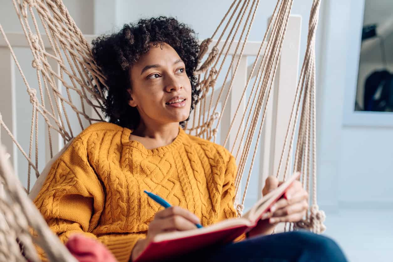 Young woman sitting in her hammock and writing in a notebook.