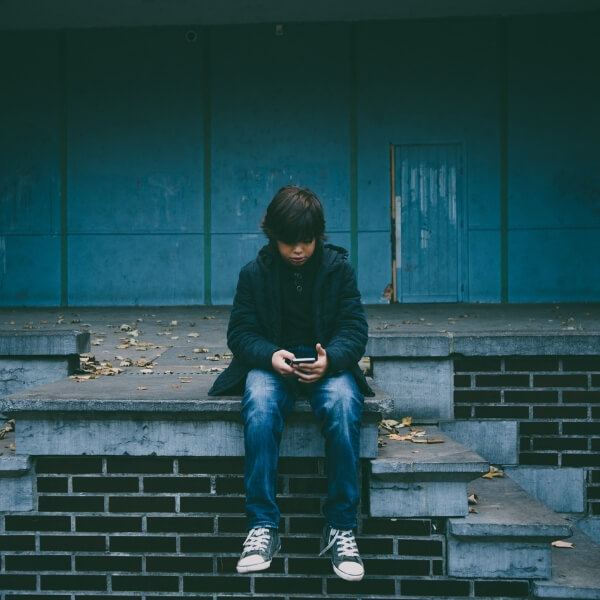 young boy sitting alone on stairs with cell phone