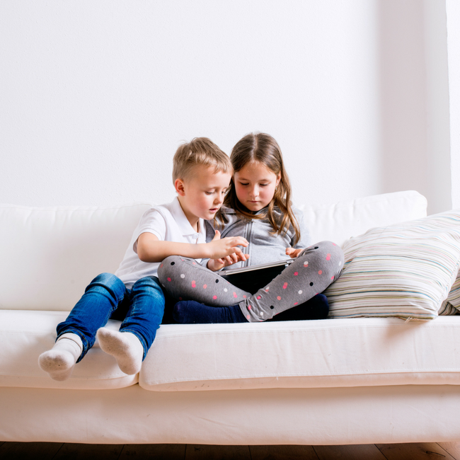 young brother and sister sitting on couch with ipad