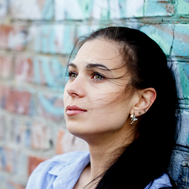 brunette woman sitting next to wall looks into distance