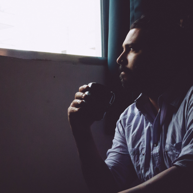man looking out window with cup of coffee