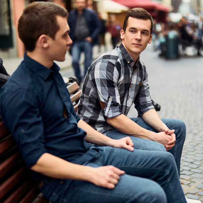 two young guy friends talking on bench outside