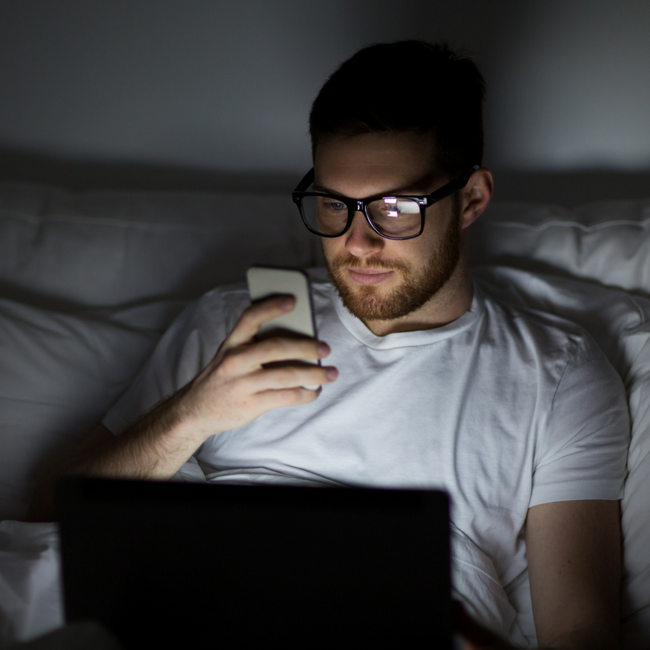 man looking at cell phone in dark bedroom