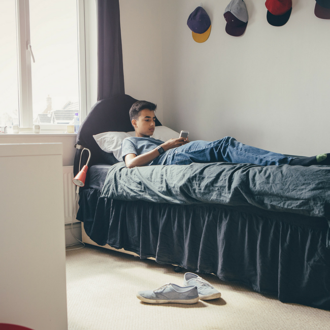 teen boy sitting on bed with smartphone