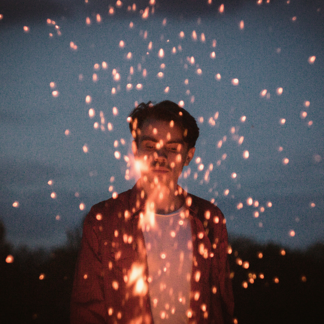young man looks into a bonfire sparks flying