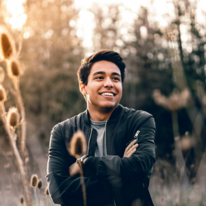happy young man with arms crossed in field