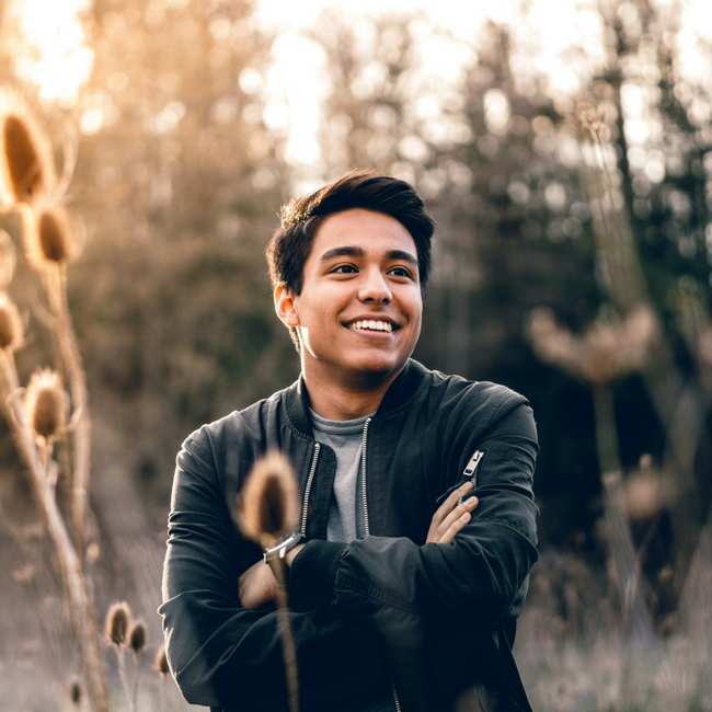 happy young man with arms crossed in field