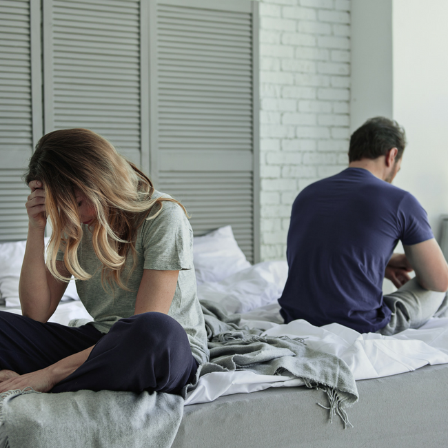 upset couple sitting on bed with backs to each other