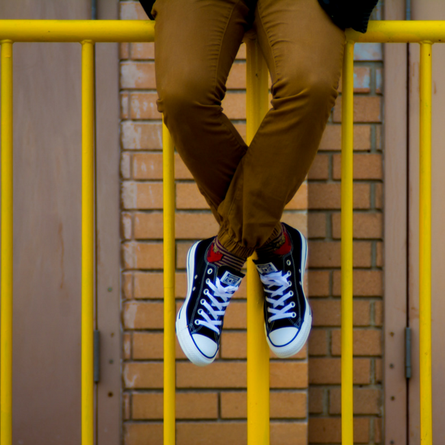 young adult male sitting on yellow fence