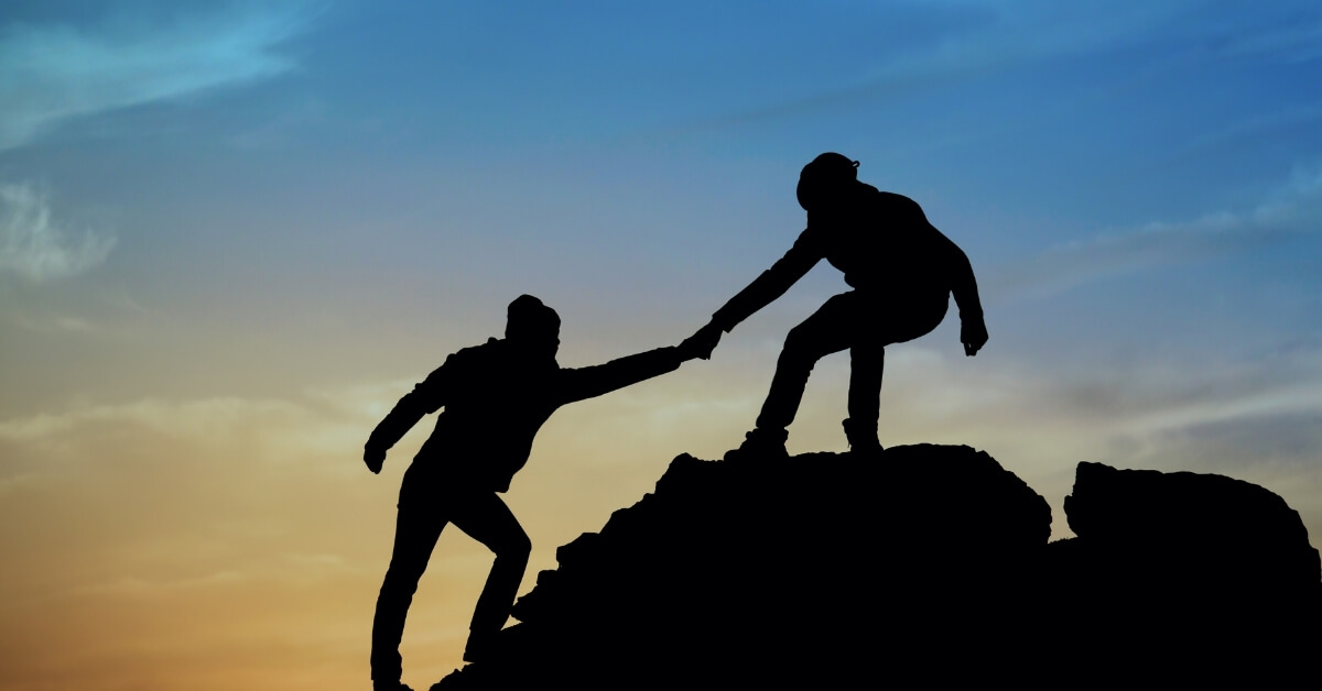 hikers helping each other up a mountain