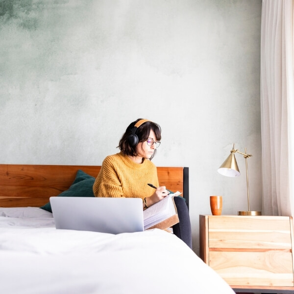 girl with headphones on in bed taking notes