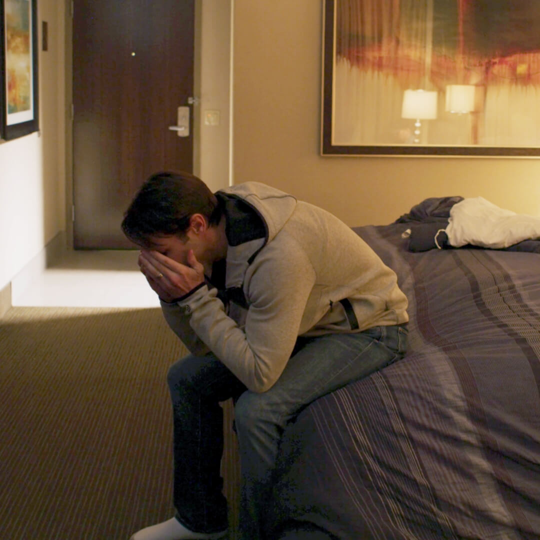 man in despair sitting on end of hotel bed