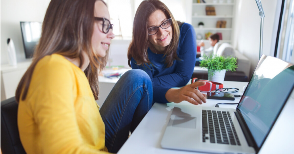 smiling mom and teen daughter point at laptop