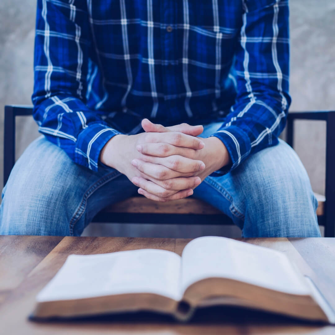 man with folded hands and open bible