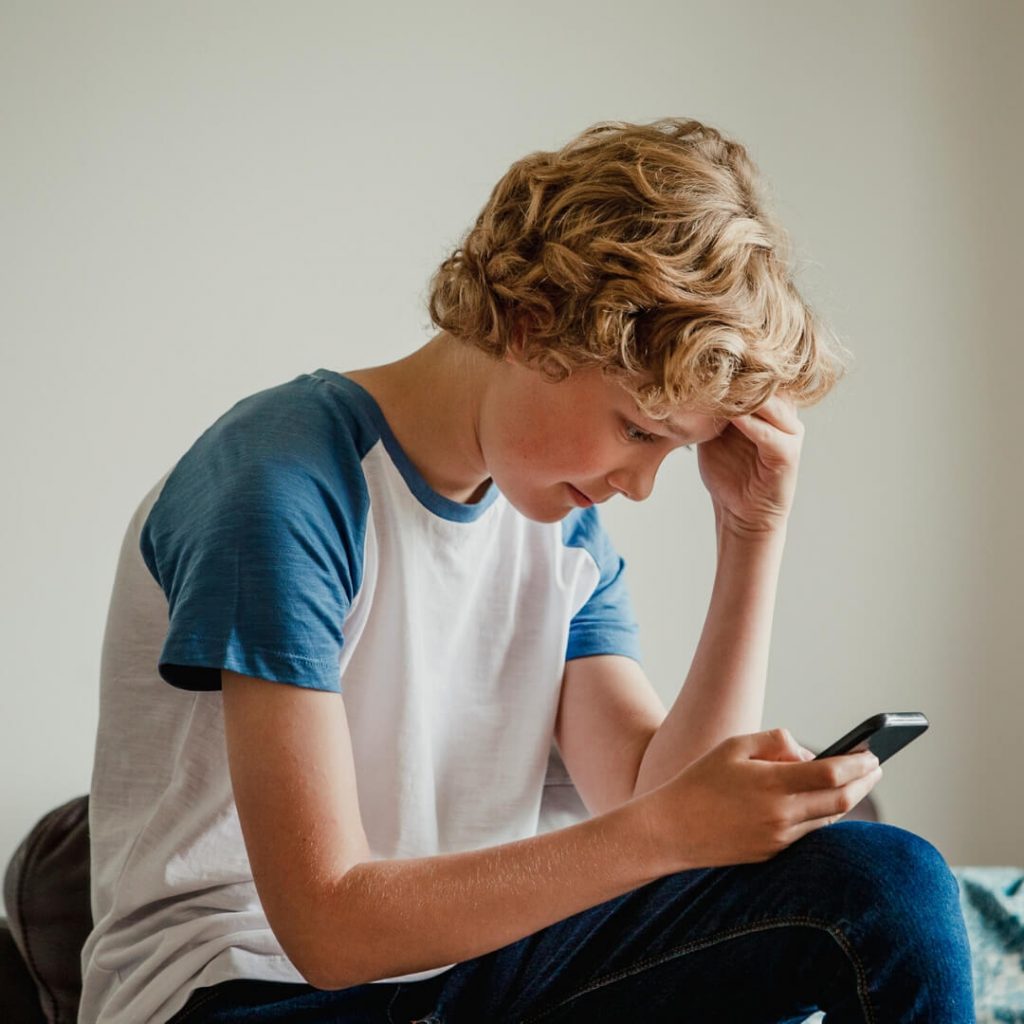 blonde teenage boy looking at phone in bed