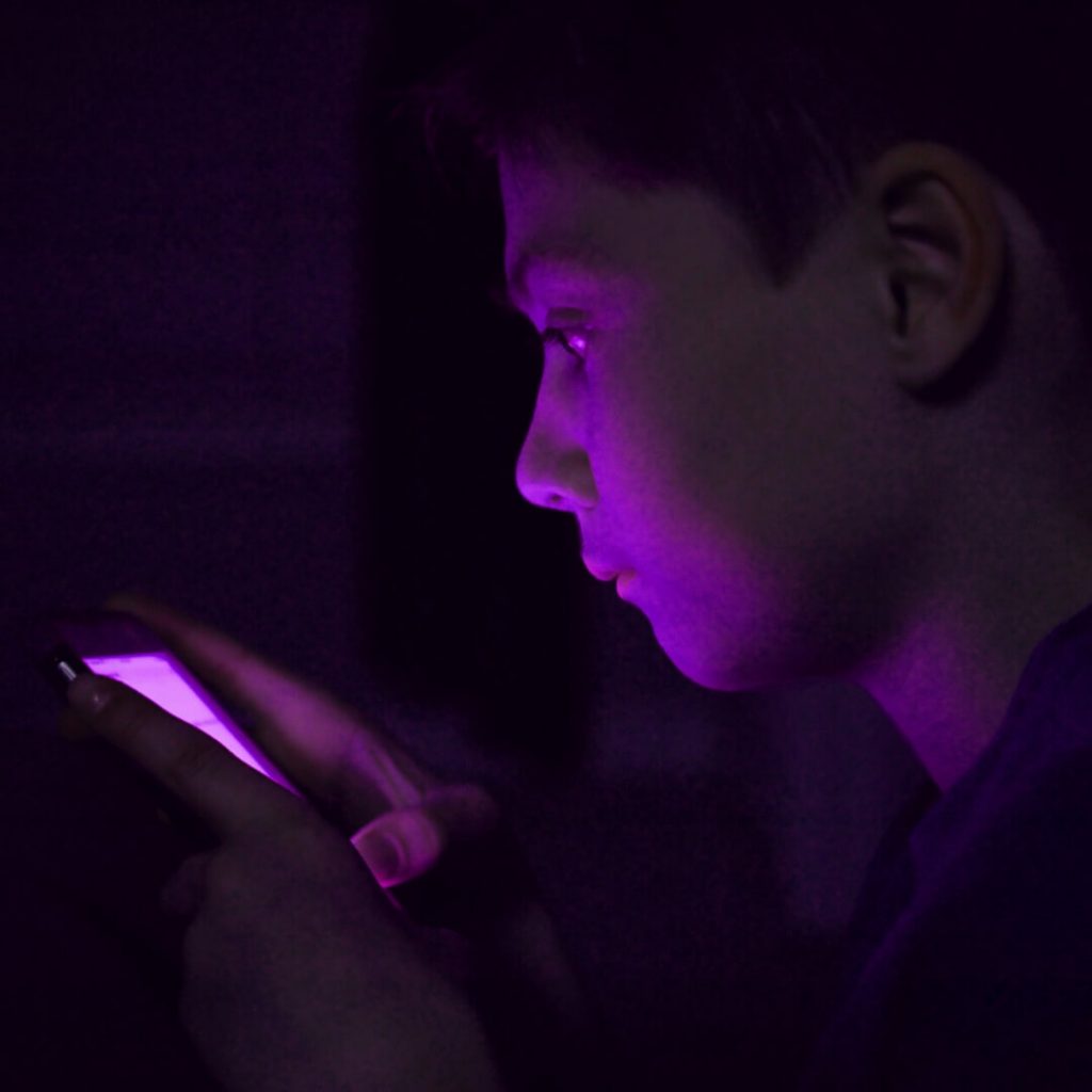 young boy looking at phone with purple screen in the dark