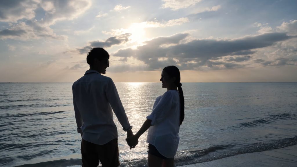 Silhouette of a young couple on a beach holding hands.
