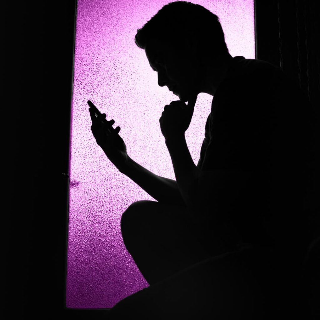 man looking at phone in dark with purple light