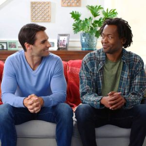 two friends sitting on couch with folded hands smiling at each other