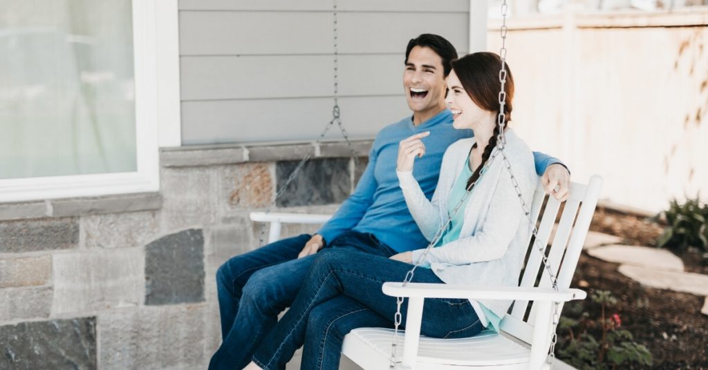 couple laughing while sitting on porch swing