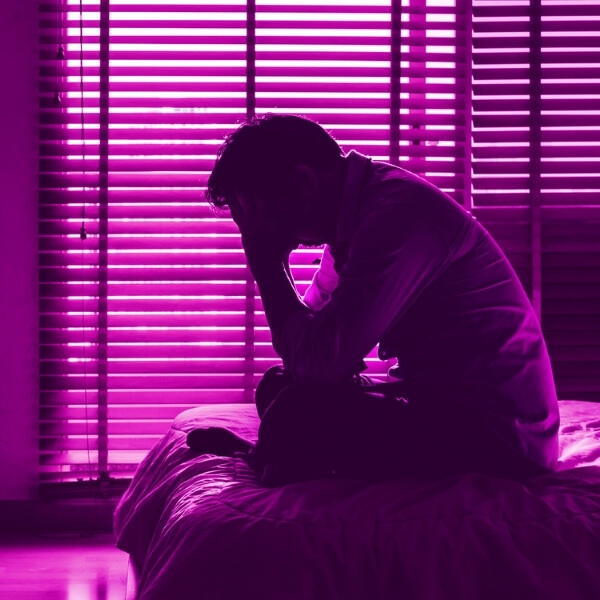 man sitting on bed with purple glow in the room